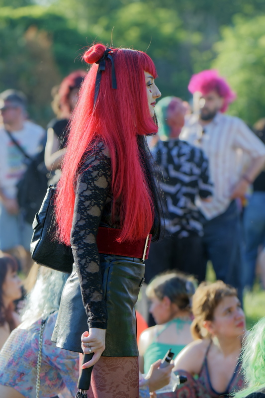 19 - Person in a crowd wearing a long-sleeved black lace top paired with a leather skirt and red corset belt